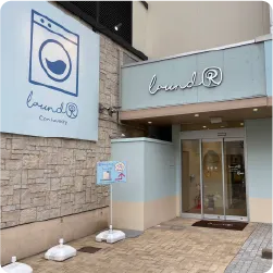 コインランドリーのパステルブルーの外観に合わせた、筆記体の立体切り文字と壁面看板