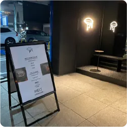 チョコレート店の壁面に設置したロゴのネオンサインと、店頭のA型看板