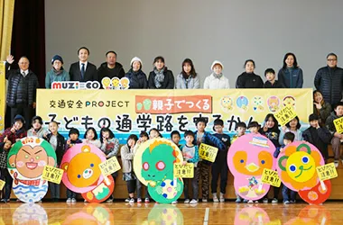 飛び出し注意看板と記念撮影する小学校の子供たちと親御さん